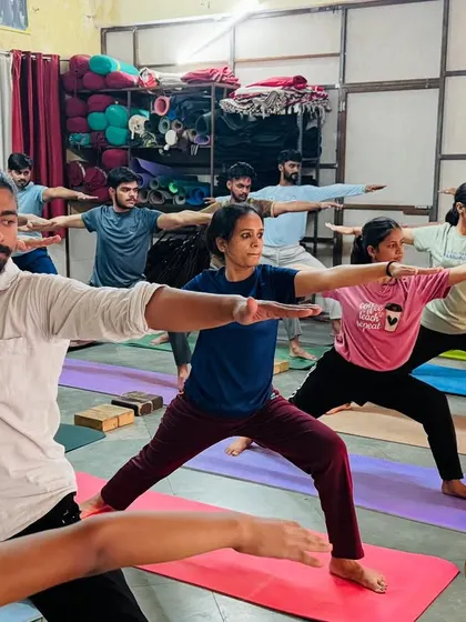 A class of students holds Virabhadrasana II (Warrior II). This powerful standing pose builds strength in the legs and focus in the mind. The collective determination is palpable.