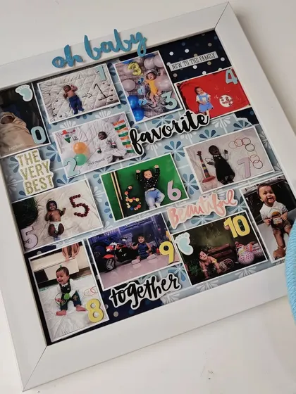 An angled shot of the baby milestone frame, highlighting the 3D effect of the photos and decorative elements inside the shadow box.