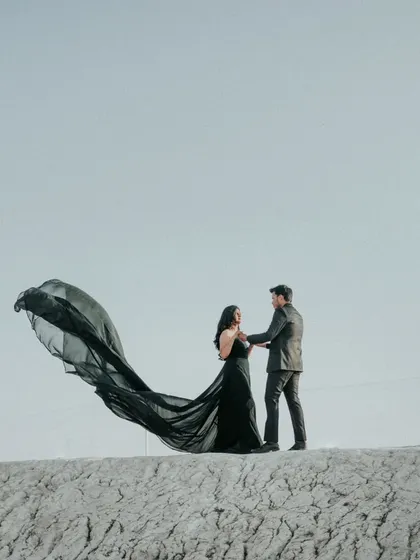 A dramatic wide shot, showing the bride's black gown flowing in the wind against the vast, open sky. This kind of epic shot is a must-have for a destination pre-wedding shoot.