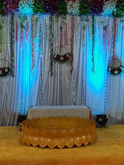 A close-up of a Haldi ceremony stage, featuring a traditional baithak and a backdrop with hanging floral wreaths and lights.