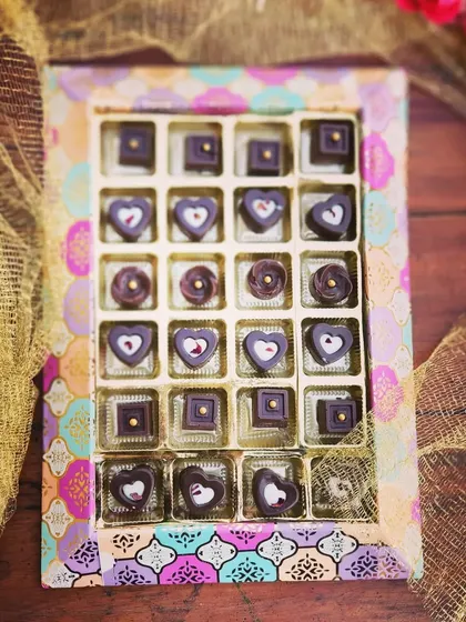 A box of our handcrafted artisan chocolates in a vibrant, traditional Indian print box. The heart and square shaped chocolates are meticulously decorated, making them a beautiful gift.