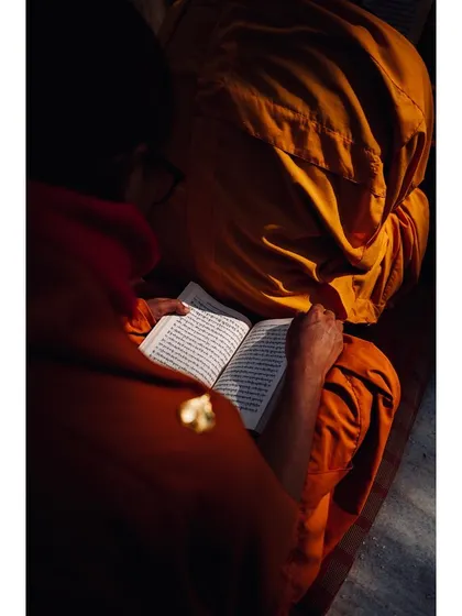 An overhead shot of a monk reading a Buddhist text, with natural light illuminating the pages. The composition draws the viewer into this intimate act of study, emphasizing the importance of scripture in the monastic life.