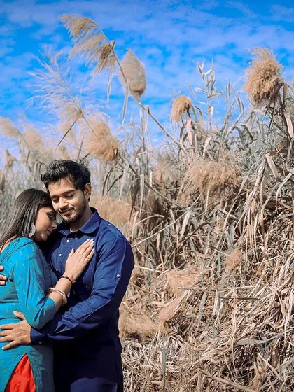 Finding a quiet moment together amidst nature. This outdoor pre-wedding photo captures an intimate embrace against a backdrop of clear blue skies and wild pampas grass, highlighting the couple's connection.