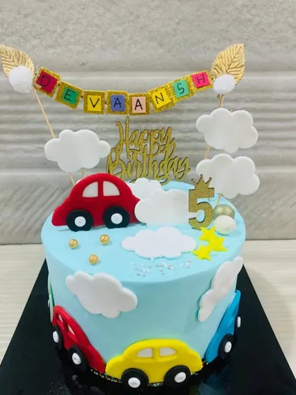 A cheerful car-themed cake for a 5th birthday. This design features a blue sky with fondant clouds and colorful cars driving around the base.