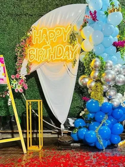 An outdoor birthday celebration with a welcome sign and a backdrop of blue and silver balloons mixed with flowers.