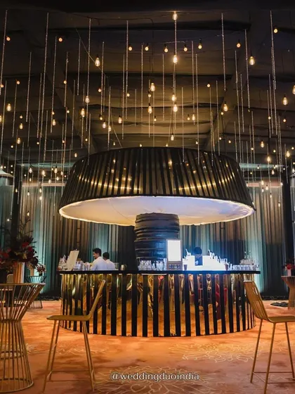 A statement bar can be the centerpiece of a great party. For this modern reception, we designed a dramatic circular bar with a black and gold aesthetic, crowned by a custom light fixture and surrounded by a ceiling of hanging bulbs to create a chic nightclub vibe.