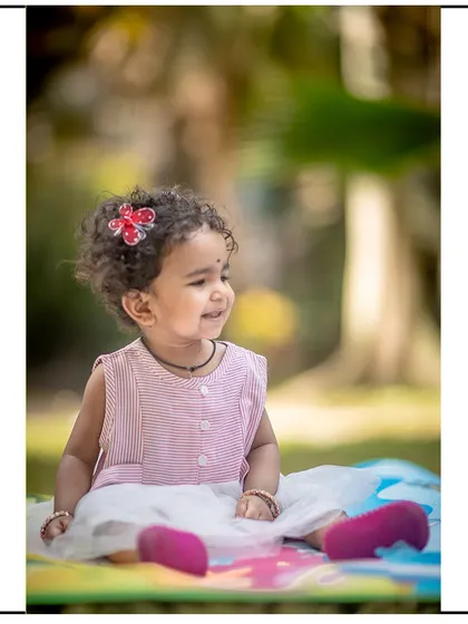 A lovely candid portrait of a little girl with curly hair, smiling during her outdoor photoshoot on a colorful play mat.