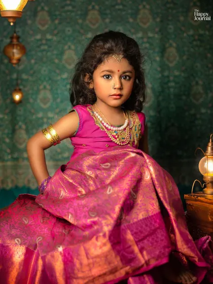 A young girl dressed in a stunning pink silk lehenga. The rich colors, traditional jewelry, and antique lanterns create a regal and artistic portrait.