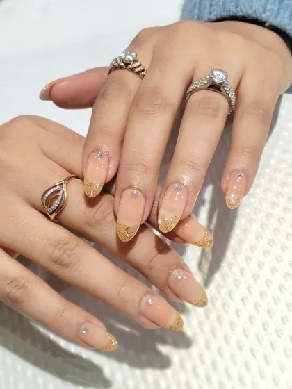 A variation of the gold glitter tip design on long, almond-shaped nails.
