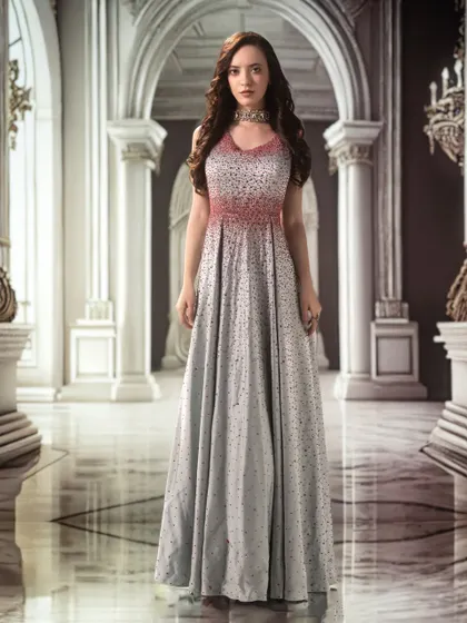 A grand palace hall, projected as a backdrop, lends a sense of scale and majesty. The lighting is kept soft and even to highlight the delicate details of the gown.