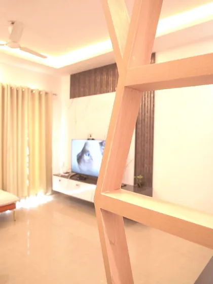 A unique perspective of the living room through a wooden geometric partition, framing the modern TV unit in the background.