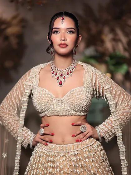 A stunning engagement or reception look featuring a contemporary white lehenga with ruby jewelry. The makeup is kept soft and glamorous to match.