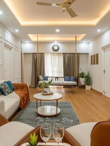 This expansive neo-classical living room is designed for effortless luxury and social gatherings. We combined a neutral palette with rich textures, including plush sofas, elegant armchairs, and warm wooden flooring, all illuminated by layered cove lighting to create an inviting ambiance. The traditional swing adds a touch of playful heritage to the modern setting.