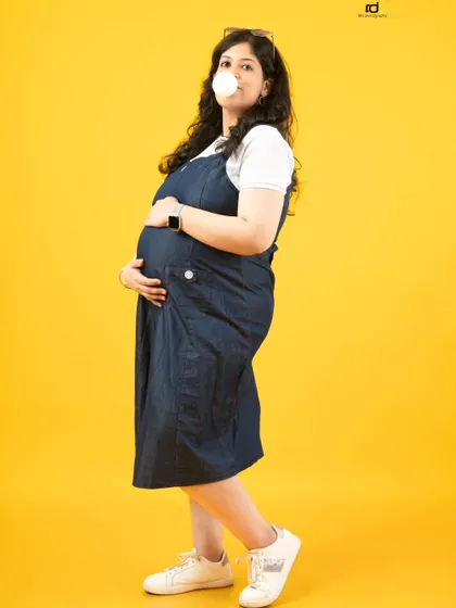 A playful and confident pose. Blowing a bubble adds a touch of fun and personality to this casual maternity shot, showing that pregnancy style can be anything you want it to be.