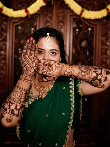 A classic peek-a-boo pose from the bride in the green saree, highlighting the intricate details of her henna.