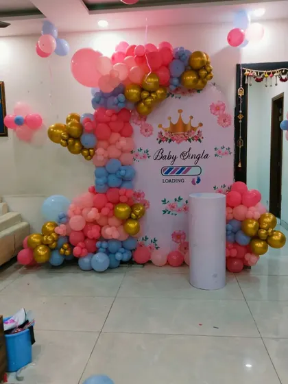 A cute baby shower decoration with a "Baby Loading" theme. The backdrop features a custom print with a crown, framed by a pink, blue, and gold balloon arrangement.