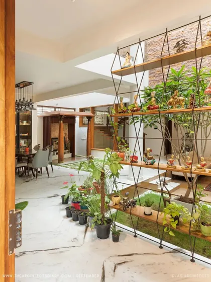 A welcoming view into the Twin Courtyard House from the entrance. The open layout immediately reveals the interconnectedness of the dining area, courtyard, and living spaces, filled with plants and natural light.