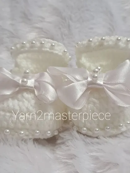 A top-down view of the white satin bow booties, highlighting the beautiful shape and the securely attached pearl and bow embellishments.
