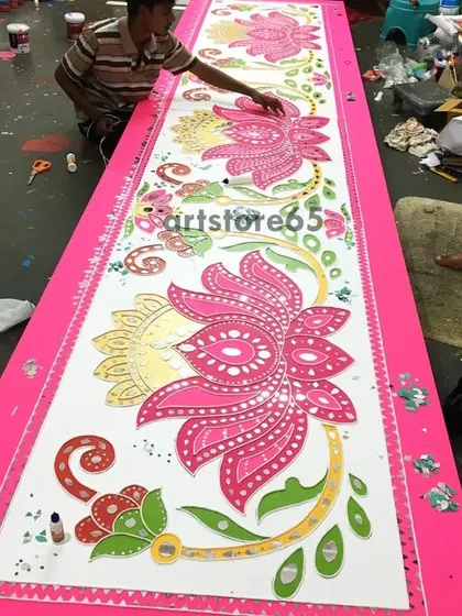 An overhead view of our artist working on a long, floral Lippan art panel. You can see the scale of the piece and the intricate process of adding details and mirrors along its length.