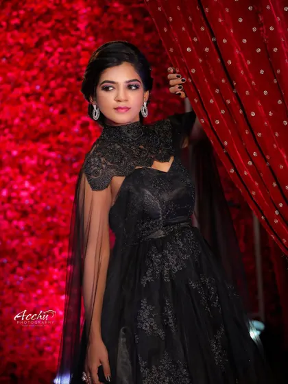 A dramatic portrait against a rich, red floral background. The black gown with a sheer cape creates a powerful silhouette, resulting in a photo that is both elegant and mysterious.