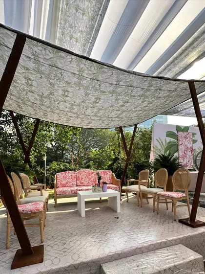 A shaded lounge area with a printed fabric canopy, pink floral sofas, and elegant chairs, offering a stylish retreat from the sun.