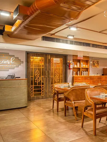 The reception area of Charcoal Restaurant features a simple, elegant desk and custom doors with traditional Indian motifs. The exposed air duct, finished in copper, is intentionally left visible as part of the industrial design aesthetic.