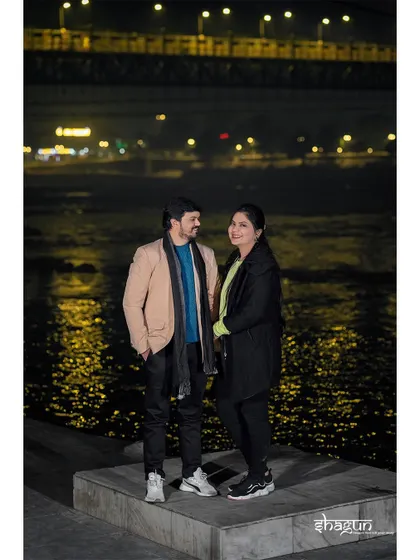 A casual, relaxed portrait by the river at night. The couple is dressed in comfortable winter wear, showing a more realistic and relatable side of their love story.