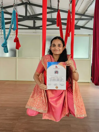 A proud graduate of our Aerial Yoga Teacher Training, holding her certificate in the hammock.