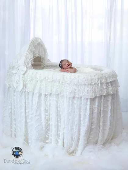 A beautiful, angelic portrait of a baby yawning in an elegant, all-white lace bassinet. This setup creates a dreamy and ethereal look.
