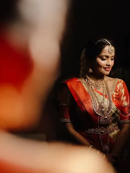 An artistic bridal portrait, with the bride's face softly lit against a dark background. The foreground blur adds depth and a sense of intimacy to the shot.