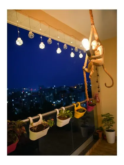This cozy balcony offers a breathtaking night view of the city. The space is made magical with whimsical string lights and a unique monkey-shaped lamp, creating the perfect blend of tranquility and urban scenery.