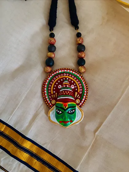 A flat-lay of the Kathakali-inspired pendant, showing the details of the hand-painting and the complementary beads on the cord.