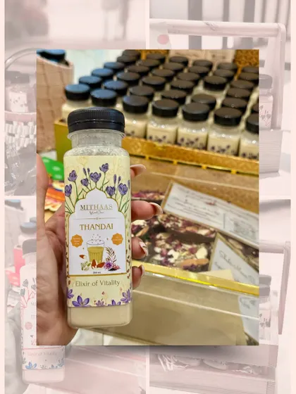 Holding up a bottle of my Thandai, the "Elixir of Vitality". In the background, you can see them being prepared for a large festive order, ready to bring joy to many.