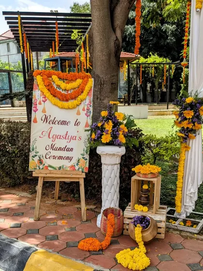 A personalized welcome sign for a Mundan ceremony. The outdoor setup is decorated with marigold flowers and floral arrangements to greet the guests.