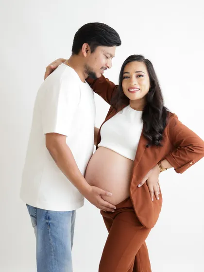 A confident and happy couple's portrait. The mom-to-be proudly displays her baby bump in a crop top and blazer, smiling alongside her partner.