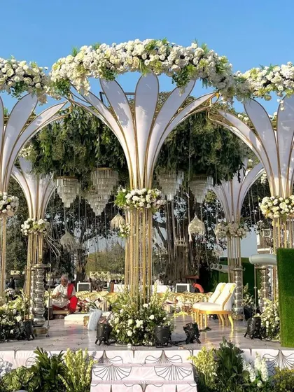 An exceptionally grand mandap with large, white, petal-like structures and hanging crystal chandeliers for a truly royal wedding.