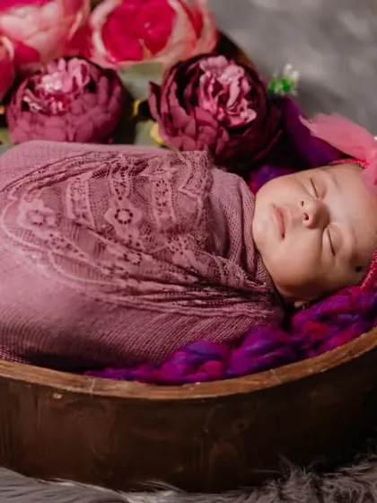 A close-up of a newborn girl, swaddled in pink and nestled in a heart-shaped prop, surrounded by flowers. A perfect portrait of pure love.