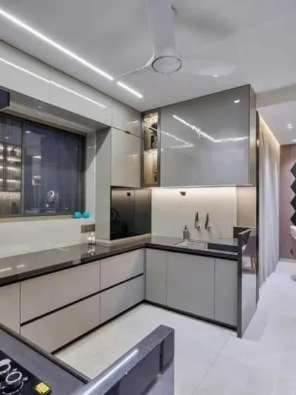 A sleek and modern modular kitchen with glossy grey cabinets and a black countertop. The glass-fronted upper cabinets and integrated lighting help to display crockery while keeping the space feeling open.