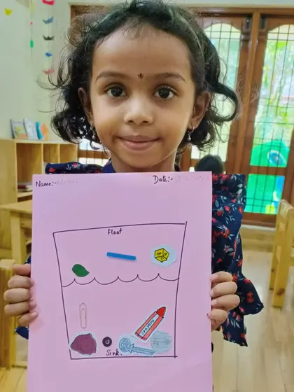 A young girl holds up her float and sink worksheet.