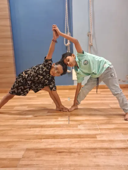 Another pair of boys hold a partner yoga pose, smiling as they help each other balance. We encourage friendship and mutual support in our classes.