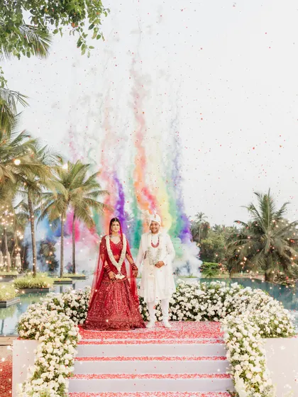 The grand finale of the varmala ceremony, with rainbow-colored smoke bombs creating a spectacular visual against the sky.