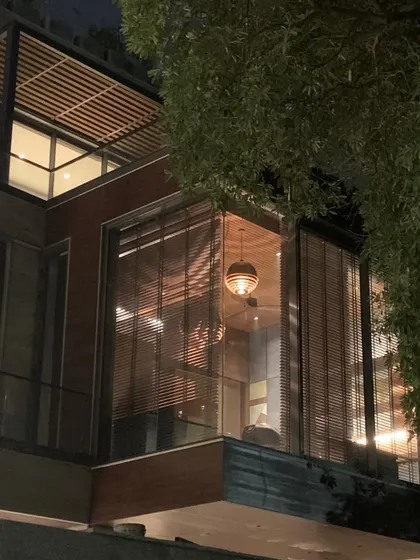 The T House study at night, seen from the exterior. The wooden blinds provide a veiled view of the interior, creating a sense of warmth and privacy while still appearing as a luminous beacon in the dark.