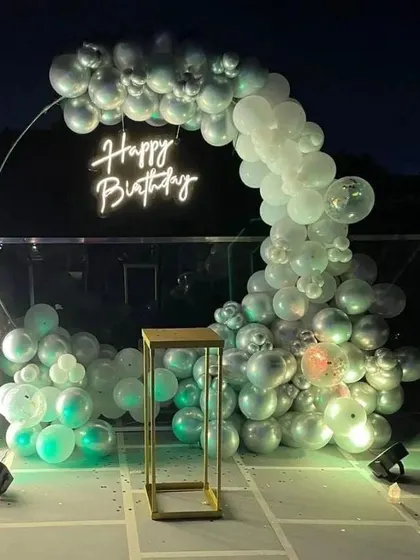 An outdoor terrace setup with a silver and white balloon crescent arch and a neon sign.