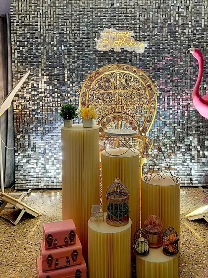 A sophisticated party setup featuring a silver sequin wall. The look is completed with elegant props like a peacock chair, flamingo statue, and a glowing butterfly, creating a chic and modern photo corner.