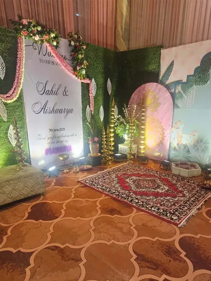 This welcome area for Sahil and Aishwarya features a personalized sign nestled among greenery and floral arrangements. The setup includes traditional lamps and a patterned rug, blending modern and classic elements beautifully.