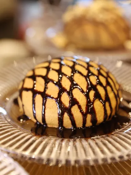 A close-up of a "chocolate shell" dessert, where a perfect sphere of cake is drizzled with rich chocolate sauce. This is a simple yet dramatic dessert that always delights.