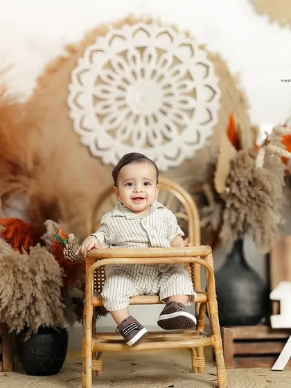 Celebrating a half birthday with a stylish boho themed sitter session. The setup features pampas grass, a rattan high chair, and a '1/2' sign to mark the milestone.