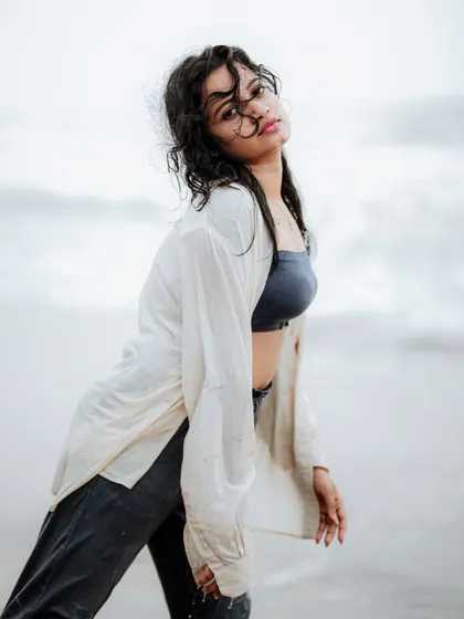 A windswept, moody portrait on the beach. The overcast sky and the model's pose create a dramatic and atmospheric fashion shot.