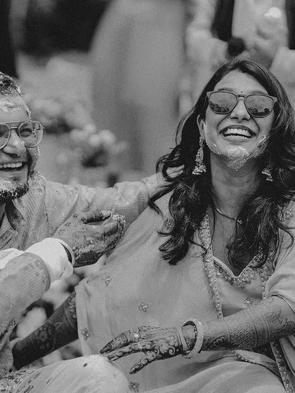A black and white photo of the couple laughing, their faces smeared with haldi, a perfect candid moment.