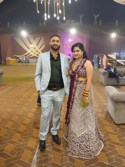 A happy client posing with her partner at a wedding. She is wearing a beautiful purple lehenga with intricate floral embroidery.